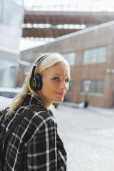 USA, New York City, Brooklyn, lächelnde junge Frau beim Musikhören mit Kopfhörern in der Stadt - BOYF01139