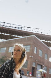 USA, New York City, Brooklyn, young woman listening to music with headphones in the city looking around - BOYF01141