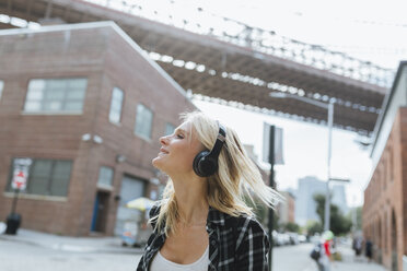 USA, New York City, Brooklyn, happy young woman listening to music with headphones in the city - BOYF01145