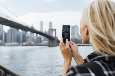 USA, New York City, Brooklyn, junge Frau am Wasser, die mit ihrem Handy ein Foto von der Brooklyn Bridge macht - BOYF01151