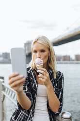 USA, New York City, Brooklyn, junge Frau steht am Wasser, isst ein Eis und macht ein Selfie - BOYF01156