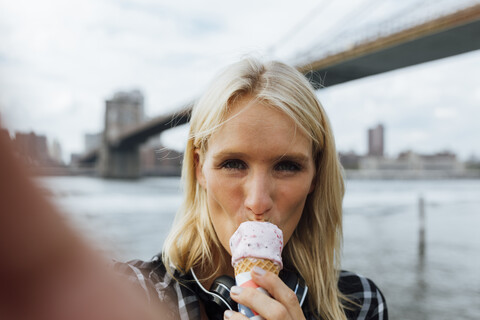 USA, New York City, Brooklyn, Selfie einer jungen Frau am Wasser, die ein Eis isst, lizenzfreies Stockfoto