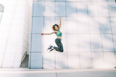 Porträt einer glücklichen jungen Frau, die auf ein Gebäude springt - OCMF00162