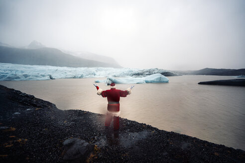 Island, Rückansicht eines als Weihnachtsmann verkleideten Mannes, der auf einem Gletscher steht und die Arme hebt - OCMF00165