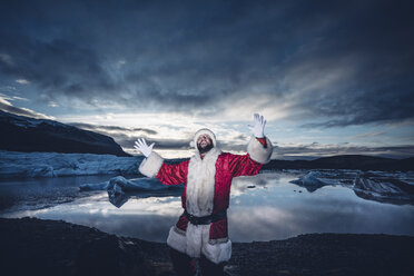 Island, ein als Weihnachtsmann verkleideter Mann steht auf einem Gletscher und hebt die Arme - OCMF00166