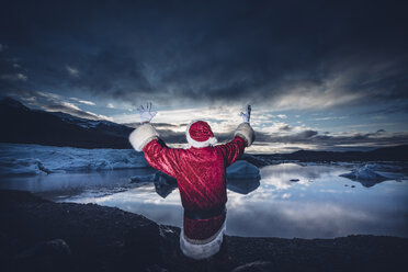 Island, Rückansicht eines als Weihnachtsmann verkleideten Mannes, der auf einem Gletscher steht und die Arme hebt - OCMF00167