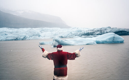 Island, Rückansicht eines als Weihnachtsmann verkleideten Mannes, der auf einem Gletscher steht und die Arme hebt - OCMF00168