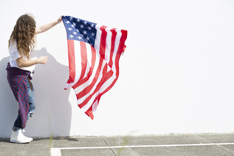 Mädchen hält amerikanische Flagge an weißer Wand, lizenzfreies Stockfoto