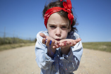 Girl blowing glitter on path in remote landscape - ERRF00177