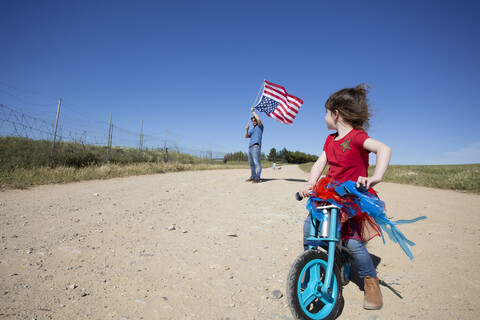 Mädchen mit Fahrrad und Mann mit amerikanischer Flagge auf Weg in abgelegener Landschaft, lizenzfreies Stockfoto