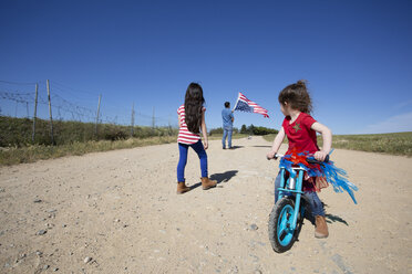 Girl with bicycle and man with American flag on path in remote landscape - ERRF00183