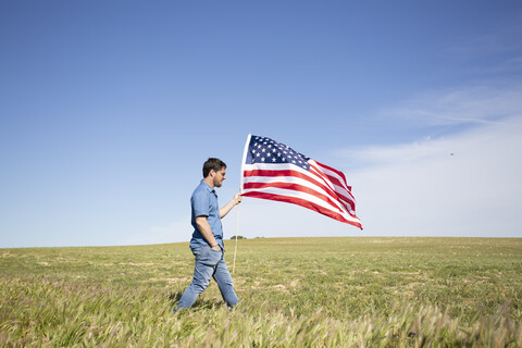 Mann mit amerikanischer Flagge auf einem Feld in abgelegener Landschaft, lizenzfreies Stockfoto