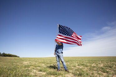 Mann hält amerikanische Flagge auf einem Feld in abgelegener Landschaft - ERRF00186