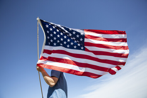 Mann hält amerikanische Flagge unter blauem Himmel, lizenzfreies Stockfoto