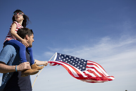 Mann mit Tochter und amerikanischer Flagge unter blauem Himmel, lizenzfreies Stockfoto