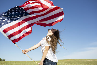 Happy girl holding American flag on field in remote landscape - ERRF00194