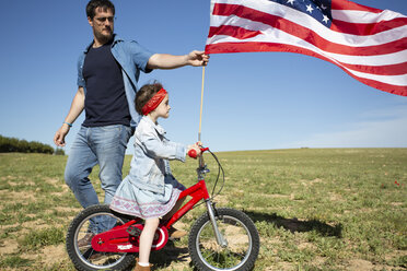 Mann und Tochter mit Fahrrad und amerikanischer Flagge auf einem Feld in abgelegener Landschaft - ERRF00200