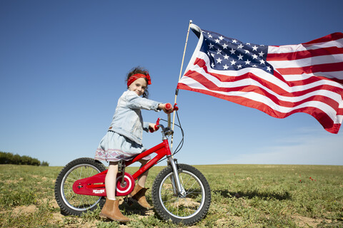 Mädchen mit Fahrrad und amerikanischer Flagge auf einem Feld in abgelegener Landschaft, lizenzfreies Stockfoto