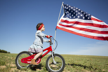 Mädchen mit Fahrrad und amerikanischer Flagge auf einem Feld in abgelegener Landschaft - ERRF00202