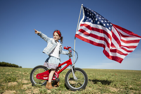 Mädchen mit Fahrrad und amerikanischer Flagge auf einem Feld in abgelegener Landschaft, lizenzfreies Stockfoto
