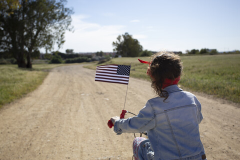 Girl with American flag riding bicycle on path in remote landscape stock photo