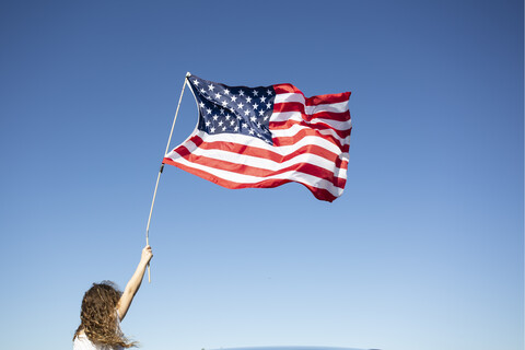 Mädchen hält amerikanische Flagge unter blauem Himmel, lizenzfreies Stockfoto