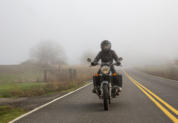 Motorradfahrerin auf einer Landstraße bei nebligem Wetter - CAVF57468