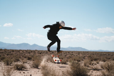 Full length of man performing stunt with skateboard on field against sky - CAVF57479