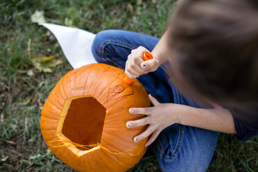 Hohe Winkel Ansicht des Mädchens Schnitzen Kürbis beim Sitzen auf Feld im Hof während Halloween - CAVF57495