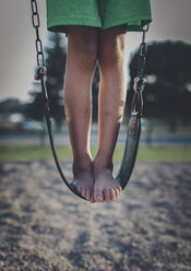 Niedriger Ausschnitt eines verspielten Jungen, der auf einer Schaukel auf einem Spielplatz steht - CAVF57501