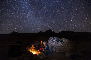 Freunde sitzen am Lagerfeuer vor einem nächtlichen Sternenfeld - CAVF57531