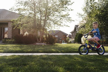 Seitenansicht eines Jungen, der auf der Straße Fahrrad fährt, inmitten eines grasbewachsenen Feldes - CAVF57533