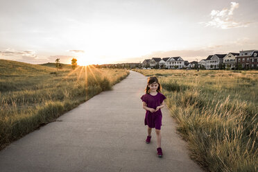 Hohe Winkel Ansicht des Mädchens zu Fuß auf der Straße gegen Häuser und Himmel bei Sonnenuntergang - CAVF57536