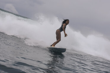 Seitenansicht einer Frau im Neoprenanzug beim Surfen auf dem Meer vor bewölktem Himmel - CAVF57545