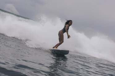 Side view of woman in wetsuit surfing on sea against cloudy sky - CAVF57545