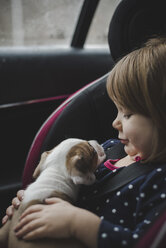 Close-up of girl with puppy sitting in car - CAVF57546