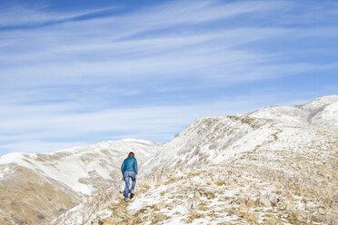 Rückansicht einer auf einen Berg kletternden Frau gegen einen bewölkten Himmel im Winter - CAVF57561