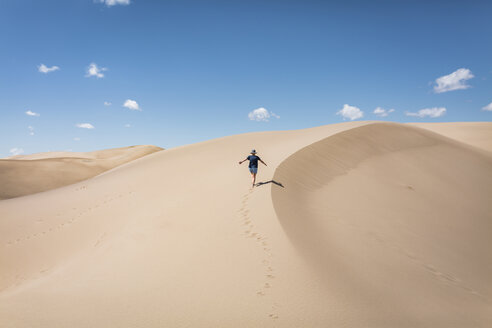 High angle view of carefree woman with arms outstretched walking on sand at Great Sand Dunes National Park during sunny day - CAVF57575