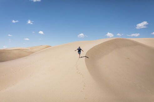 Hohe Winkel Ansicht der sorglosen Frau mit ausgestreckten Armen zu Fuß auf Sand in Great Sand Dunes National Park während des sonnigen Tages - CAVF57575