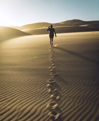 Rückansicht einer unbekümmerten Frau, die bei Sonnenuntergang im Great Sand Dunes National Park über den Sand läuft - CAVF57576