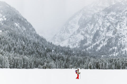 Seitenansicht einer Frau mit Rucksack beim Wandern auf einem schneebedeckten Feld, lizenzfreies Stockfoto