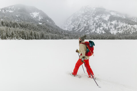 Seitenansicht einer Frau mit Rucksack beim Wandern in einer verschneiten Landschaft, lizenzfreies Stockfoto