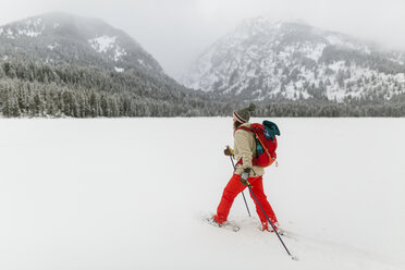 Side view of woman with backpack hiking on snow covered landscape - CAVF57585