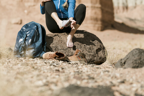 Niedriger Ausschnitt eines Wanderers, der seine Socken auszieht, während er auf einem Felsen in der Wüste sitzt, lizenzfreies Stockfoto