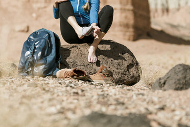 Niedriger Ausschnitt eines Wanderers, der seine Socken auszieht, während er auf einem Felsen in der Wüste sitzt - CAVF57594