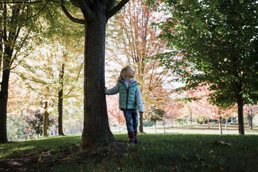 Mädchen in voller Länge mit Blick nach oben, während sie im Herbst an einem Baum im Park steht - CAVF57603