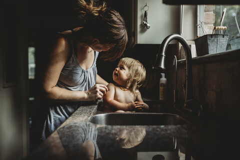 Mutter badet ihre Tochter ohne Hemd in der Küchenspüle zu Hause, lizenzfreies Stockfoto