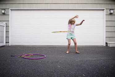 Mädchen, das mit einem Plastikreifen spielt, während es auf der Straße vor einer Garage steht - CAVF57649