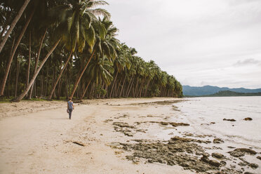 Rückansicht einer Frau, die am Strand zwischen Kokosnusspalmen spazieren geht, gegen den Himmel - CAVF57652