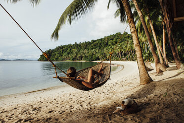 Young woman resting in hammock by dog at beach - CAVF57665